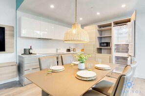 Una cocina moderna con armarios blancos, una mesa de comedor lista para cuatro personas y un lámpara colgante.