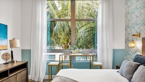 A hotel room with a large window, a bed, a bedside table, a lamp, and a view of palm trees. - Rooftop Pool & Hot Tub| Hollywood Beach Boardwalk (Hollywood)