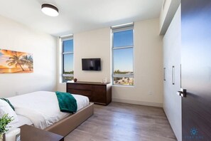 A modern bedroom with a bed, a TV, a desk, and a window with a view. - Rooftop Pool + Hot Tub|Hollywood Beach|Near Beach (Hollywood)