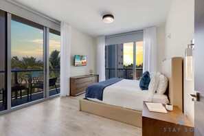 Relax in a spacious room with a large bed, flat-screen TV, and balcony overlooking palm trees.