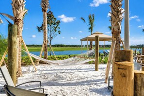 A beach with a hammock, wooden chairs, a wooden structure, and a view of the water.