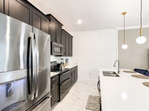 A modern kitchen with stainless steel appliances, dark cabinetry, and a white countertop.