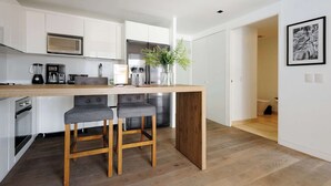 A modern kitchen with white cabinetry, a wooden island, two bar stools, a stainless steel refrigerator, and a potted plant. - w* | Modern 1BR in New Building in Roma Norte (Ciudad de México)