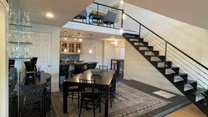 A spacious living area with a dining table, a staircase, and a kitchen in the background. - Beautiful 4 Bedroom River Front House in Downtown (Augusta)