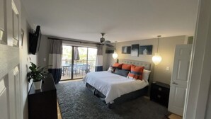A modern bedroom with a large bed, a ceiling fan, a TV mounted on the wall, and a sliding glass door leading to an outdoor area. - Beautiful 4 Bedroom River Front House in Downtown (Augusta)
