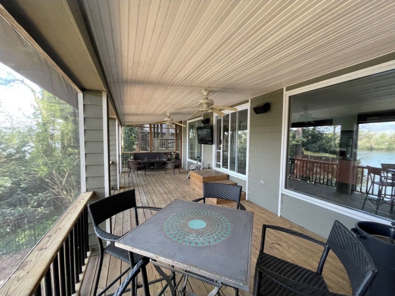 Une terrasse extérieure couverte, équipée d’une table et de chaises, d’un téléviseur fixé au mur et offrant une vue sur l’extérieur.