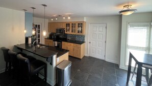 A modern kitchen with a central island, wooden cabinets, and a built-in microwave. There are bar stools and a trash can near the island. - Beautiful 4 Bedroom River Front House in Downtown (Augusta)