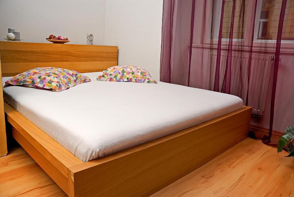 A single bed with a wooden frame, white bedding, and colorful floral pillows.