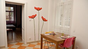 Een eetgedeelte met een houten tafel, een roze stoel en een raam met dunne gordijnen.