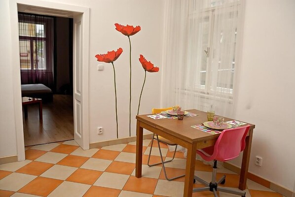 Un comedor con una mesa de madera, una silla rosa y una ventana con cortinas traslúcidas.
