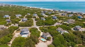 An aerial view of a coastal residential area with houses, a swimming pool, and a beach. - OCEANSIDE:  Private Pool, beautiful home on full acre lot! (Corolla)