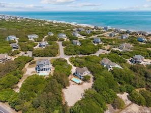 An aerial view of a coastal residential area with houses, a swimming pool, and a beach.