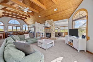 A spacious living area with a stone fireplace, a television, and a large window overlooking the outdoors.