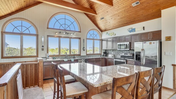 A spacious kitchen with a large island, wooden cabinets, and a view of the outdoors through arched windows. - OCEANSIDE:  Private Pool, beautiful home on full acre lot! (Corolla)