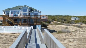 Ein Strandgrundstück mit einer Holzpromenade, die zu einem großen, mehrstöckigen Haus mit Balkon führt.