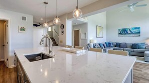 A modern kitchen with a marble island, pendant lighting, and a staircase leading to another level.