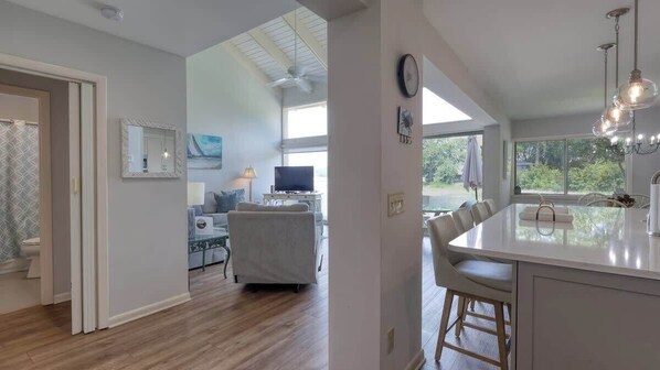 A modern kitchen with a large island, a dining area with chairs, and a television in the background.
