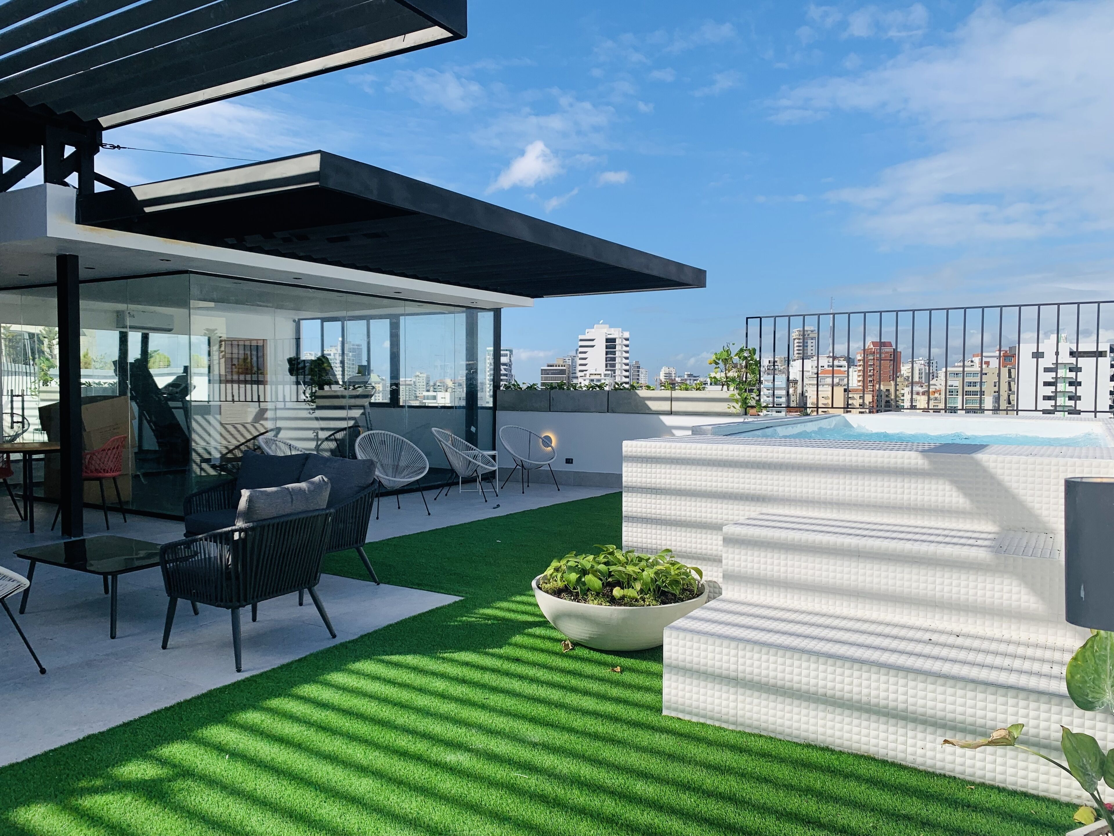 A modern outdoor terrace with a glass enclosure, seating area, and a hot tub.