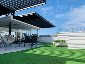 Une terrasse extérieure moderne, dotée d’une véranda en verre, de mobilier d’extérieur et d’une pelouse bien entretenue.