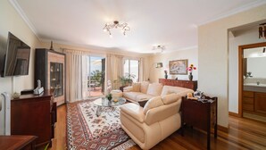 Un salon avec un canapé, une table basse et un téléviseur. Il y a une fenêtre avec des rideaux, une plante et un tableau au mur.