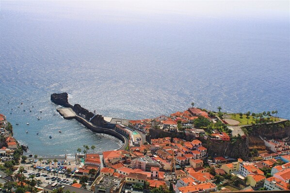 Un pueblo costero con un acantilado destacado, un puerto deportivo con barcos y una mezcla de edificios residenciales con tejados rojos.