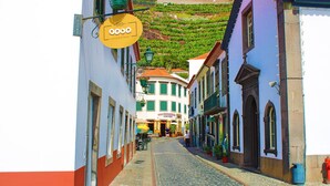 Une ruelle étroite pavée, bordée d’immeubles, une enseigne indiquant « Ponca & Tapas », et une colline en arrière-plan.