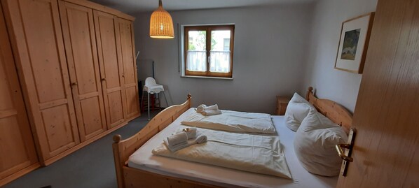 Ein Schlafzimmer mit einem hölzernen Bett, einem Fenster, einem Kleiderschrank und einer Pendelleuchte.