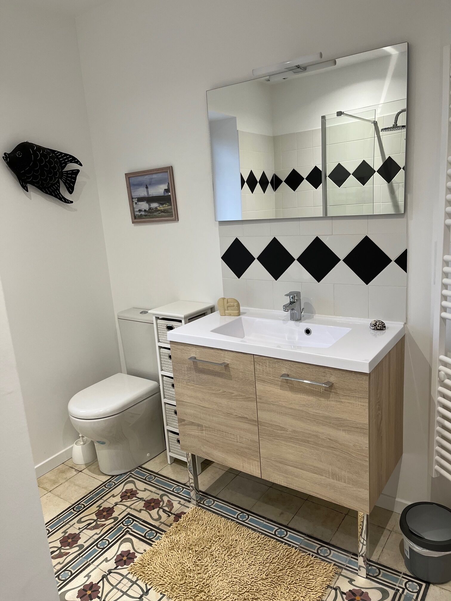 Ein modernes Badezimmer mit einem weißen Waschbecken, einem Holz-Waschtisch und einem großen Spiegel.