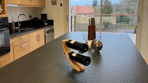 Una cocina moderna con armarios de madera, una encimera negra y una estantería con dos botellas de vino.