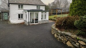 A white house with a stone foundation, a covered patio, and a stone wall. - Green Stile Cottage (Windermere)