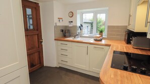 A modern kitchen with white cabinets, a wooden countertop, a built-in oven, and a window providing natural light. - Green Stile Cottage (Windermere)