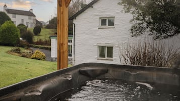 Un jacuzzi dans un jardin, avec une maison blanche en arrière-plan.