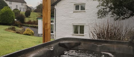 A hot tub in a garden with a white house in the background.