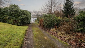 A narrow, unpaved path leading to a white building surrounded by dense greenery and trees. - Green Stile Cottage (Windermere)