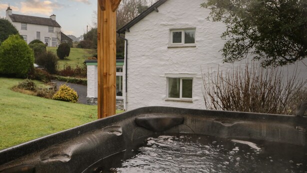 A hot tub in a garden with a white house in the background. - Green Stile Cottage (Windermere)