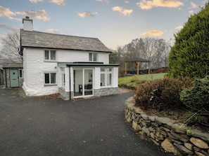 A white house with a stone foundation, a covered patio, and a stone wall. - Green Stile Cottage (Windermere)