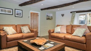 A cozy living room with two leather sofas, a wooden coffee table, and framed pictures on the walls. - Green Stile Cottage (Windermere)