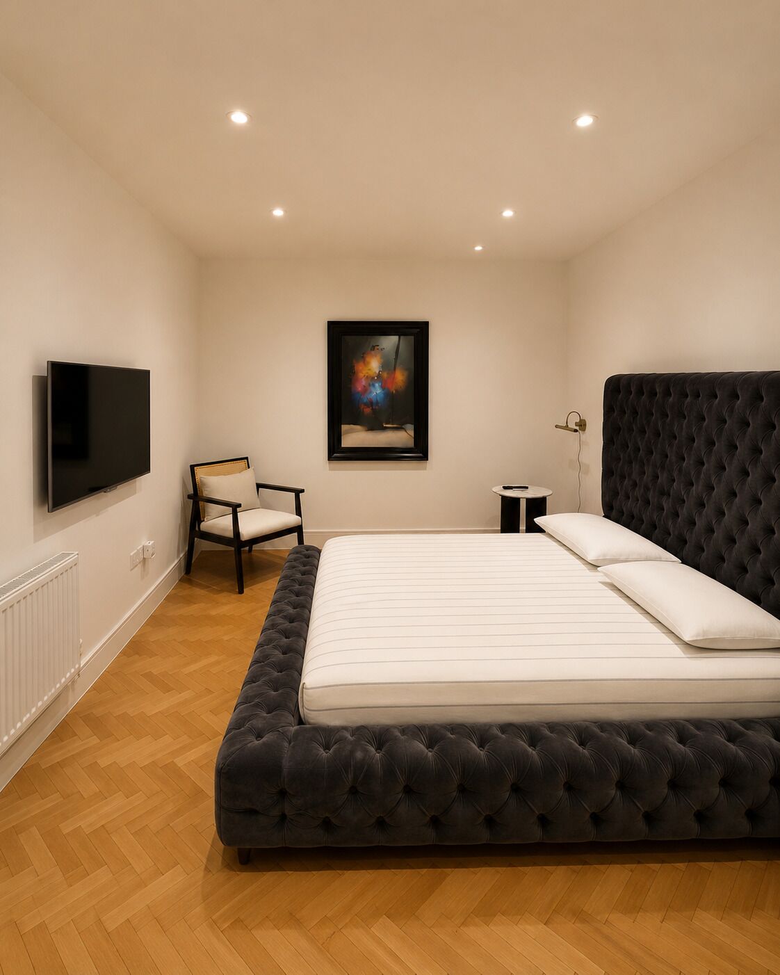A bedroom with a large bed, a chair, a TV, and a painting on the wall.