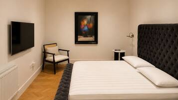 A bedroom with a large bed, a chair, a TV, and a painting on the wall.