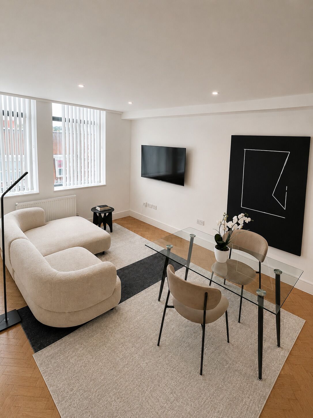 A modern living room with a sofa, chairs, a glass coffee table, a TV, and a large abstract painting.
