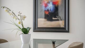 A white orchid in a white pot on a glass table with a framed abstract painting in the background.