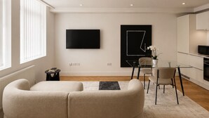 Una sala de estar moderna con un sofá, un televisor de pantalla plana, un comedor con mesa y sillas, y una zona de cocina.