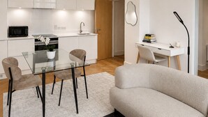 Una sala de estar moderna con una mesa de vidrio, dos sillas, un sofá y un escritorio con una lámpara.