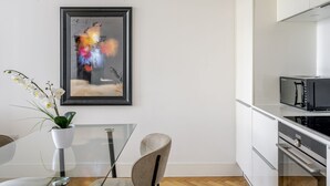 Una cocina moderna con gabinetes blancos, un microondas y una mesa de comedor de vidrio con una silla.