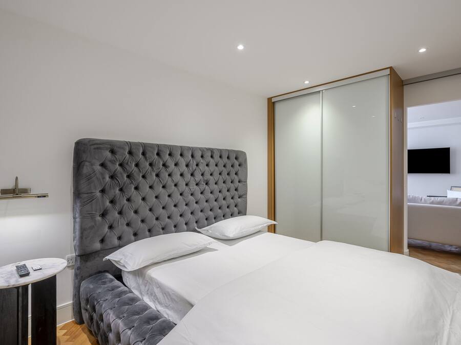 Een moderne slaapkamer met een gestoffeerd hoofdeinde, een nachtkastje met een afstandsbediening, en een groot bed met witte beddengoed.