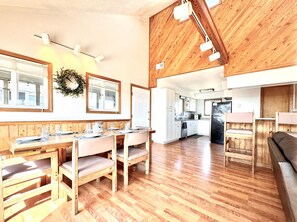 Cozy living and dining area with a high ceiling, wooden beams, and a central dining table for four.