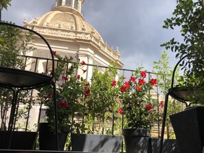 A view of a building with a dome and columns, surrounded by potted plants and a metal railing. - A romantic terrace on the Badia (Catania)