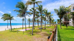 A beach view with palm trees, a grassy area, and a building with balconies. - Waiwai Cumbuco pé na areia por Carpediem (Caucaia)