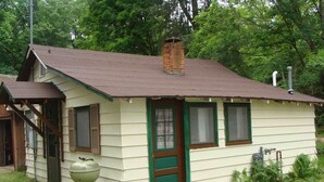 A small, single-story house with a chimney, a front door, and a small porch. - On North Twin Lake- Northern Exposure Rentals "Minnow Bucket" (Phelps)