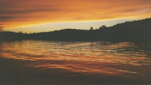 A sunset over a body of water with a silhouette of a hill in the background. - On North Twin Lake- Northern Exposure Rentals "Minnow Bucket" (Phelps)
